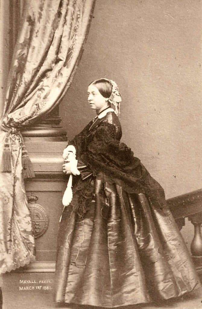 Gammal sepiafotografi av kvinna i 1800-tals klädsel med elegant pose.