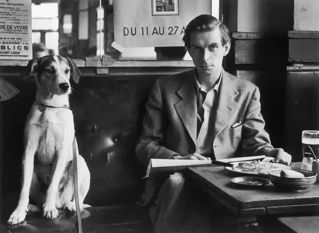 Den unge Leo Zimmerman i kostym vid ett kafébord, med en stor hund sittande upprätt tätt intill.