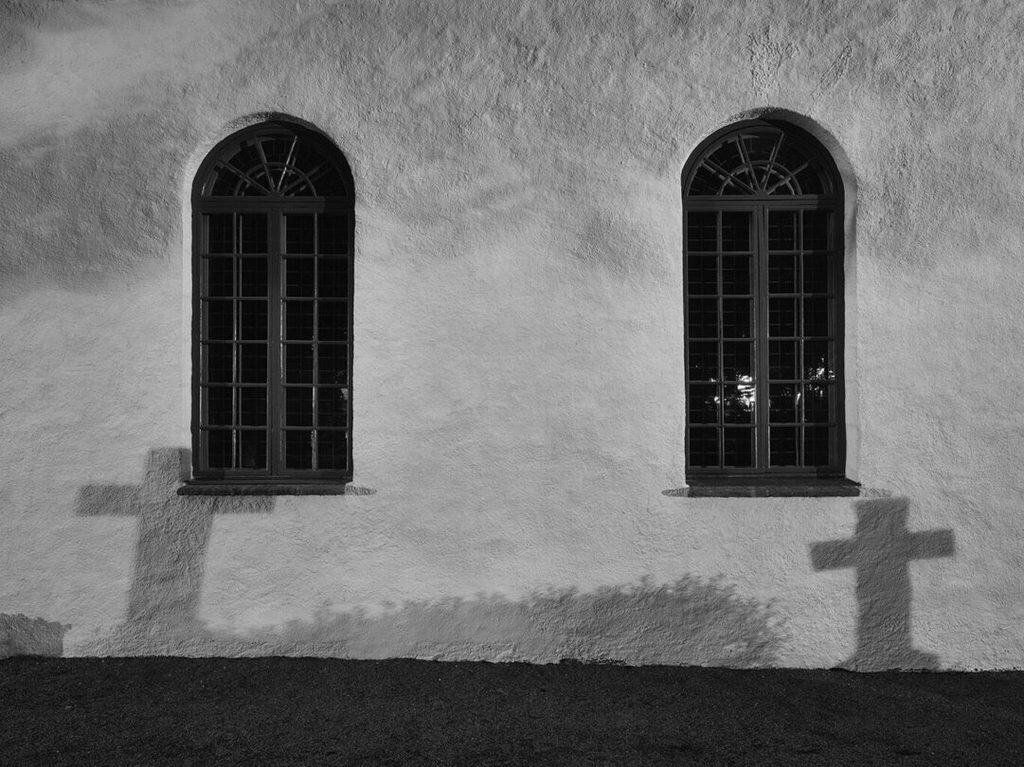 Två valvfönster i en vitputsad kyrkvägg kastar korsformade skuggor i kvällsljuset