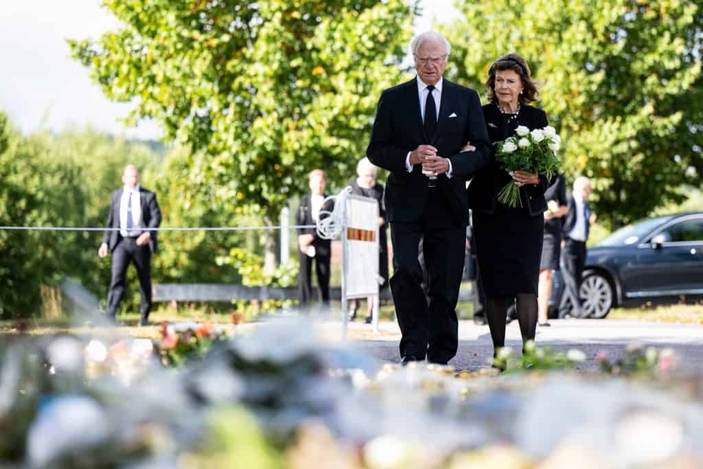 Kungaparet går arm i arm mot blomsterhavet utanför Brinellskolan i Fagersta, drottningen med vita rosor.