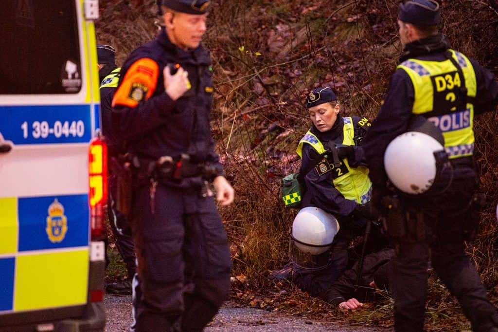 Poliser vid en piketbuss i skymningen, en av dem håller ner en person i vägkanten.