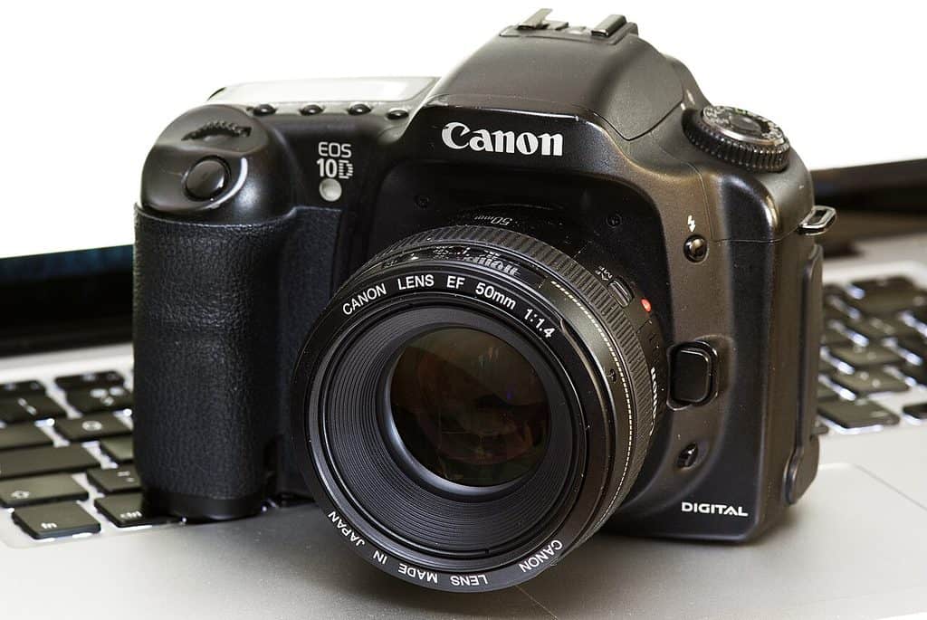 Svart Canon EOS 10D snett framifrån, stående på ett bärbart datortangentbord mot vit bakgrund. Ett Canon EF 50 mm 1:1,4-objektiv är monterat, texten EOS 10D står på husets vänstra framsida och ordet DIGITAL nere till höger