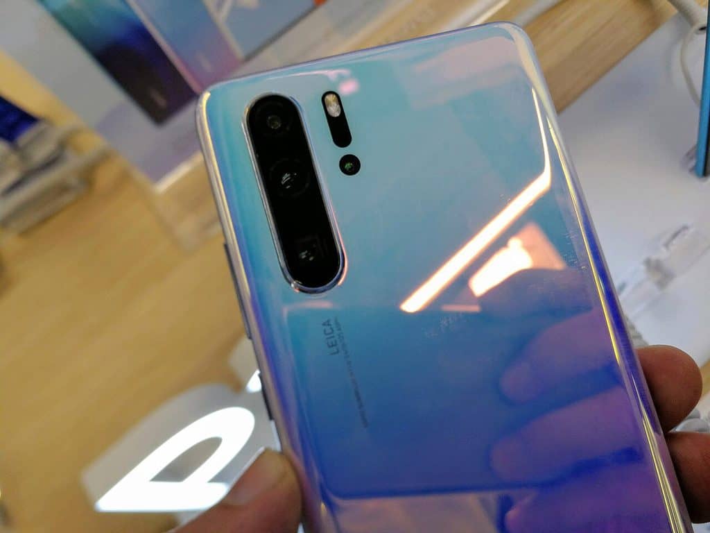 En hand som håller en Huawei P30 Pro med skimrande blåvit baksida och ett lodrätt kameraparti med flera objektiv.