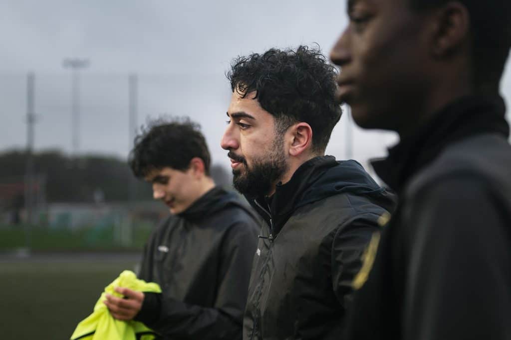 Shahrdad i profil mellan två lagkamrater på fotbollsträningen