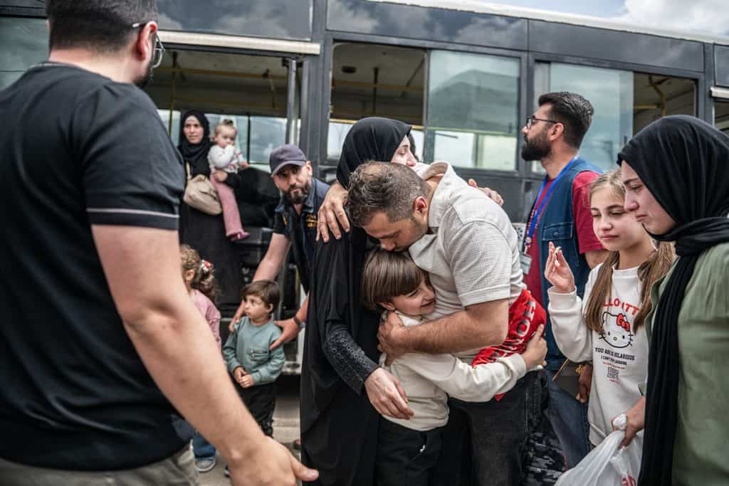 En man kramar en kvinna och ett barn vid bussen när återvändande familjer möts
