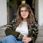 Lisa Hallgren sitter på en stentrappa i stickad kofta och glasögon