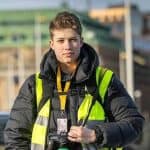 Philip Kangas i gul reflexväst med presskort och två kameror, stadsmiljö bakom honom.
