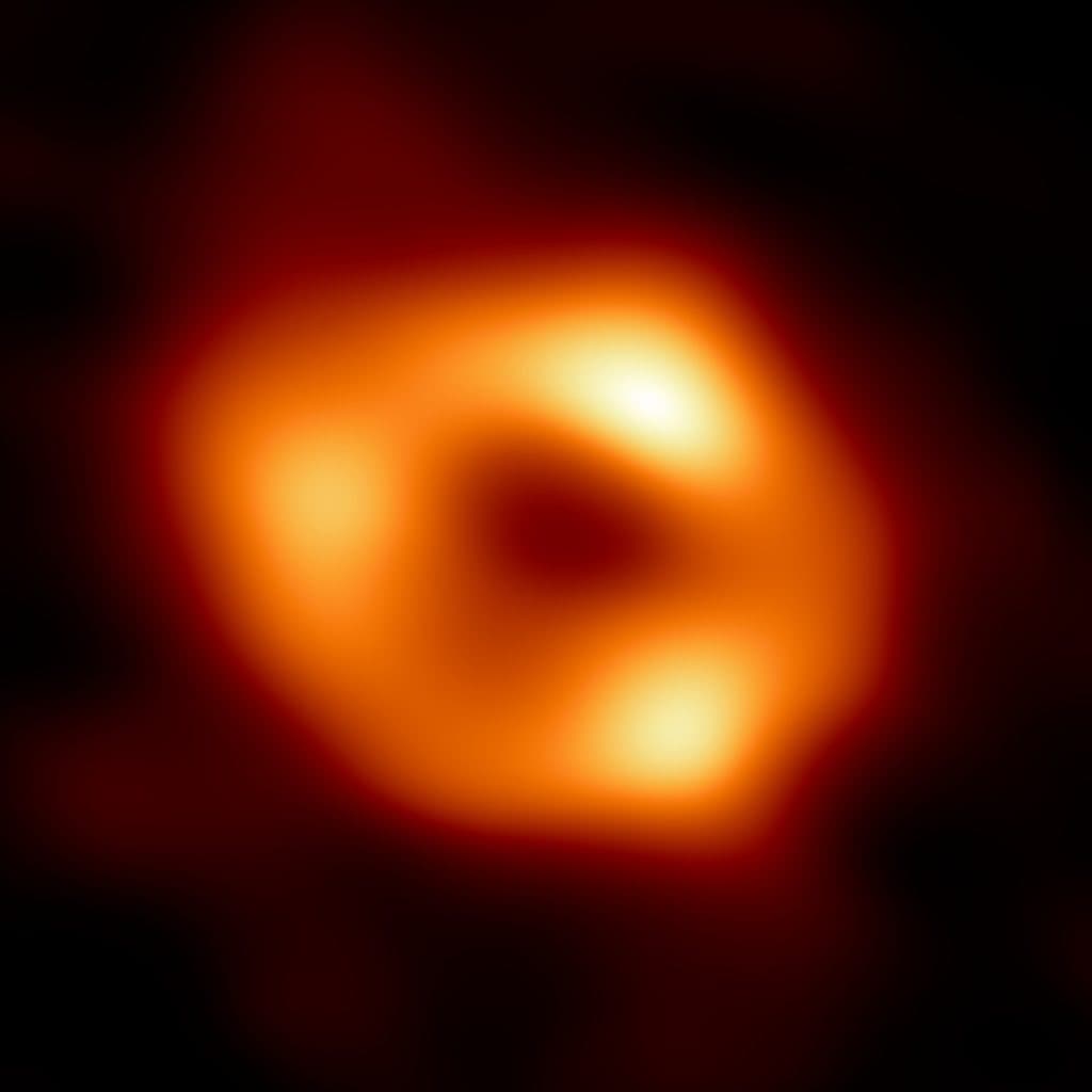 En suddig orange ring mot mörk bakgrund med en mörk fläck i mitten. Ringen har tre ljusare partier, två till höger och ett till vänster.